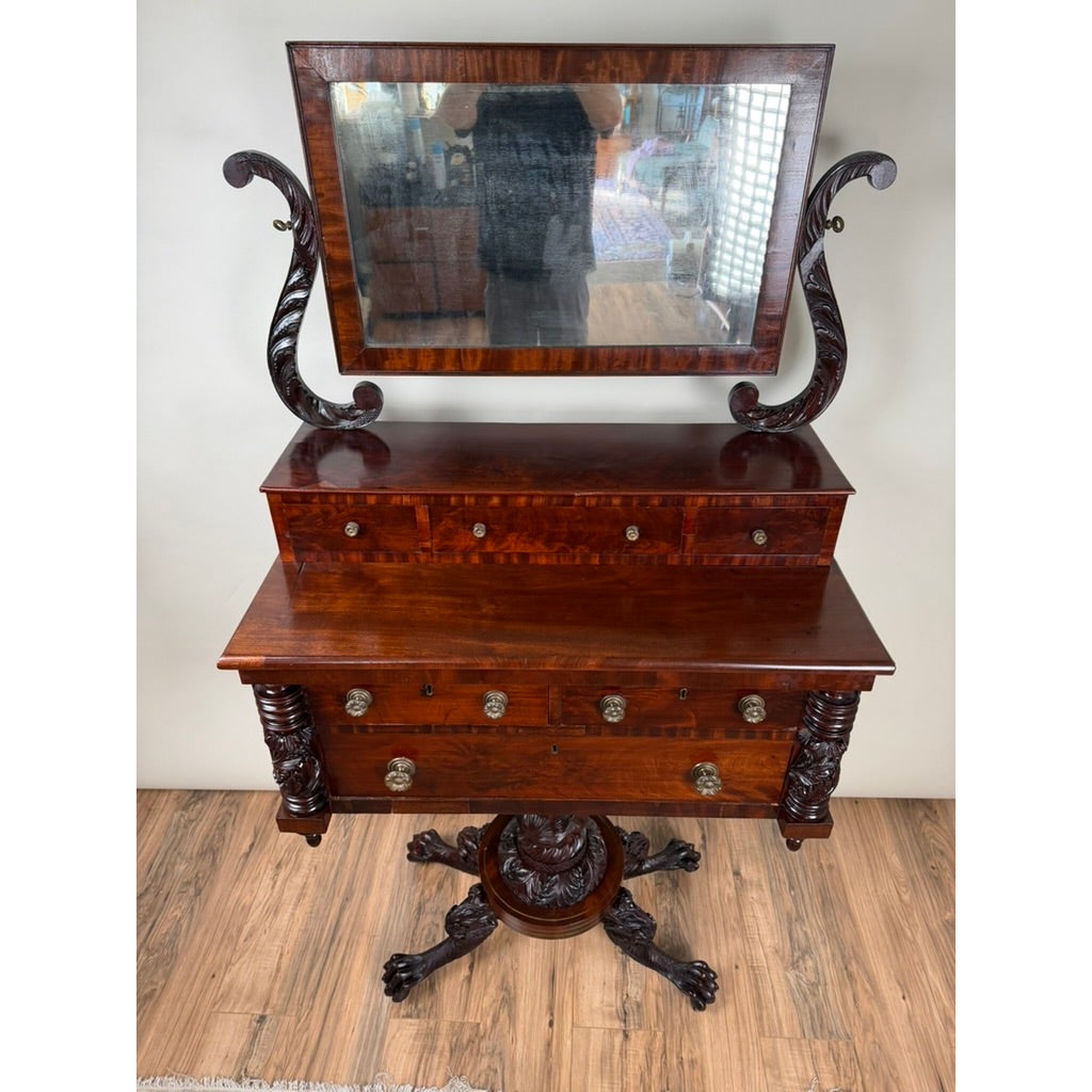 American Classical Carved Mahogany Dressing Table with Original Mirror, Probably New York, c. 1825–1835, featuring a central pedestal base, carved columns, several drawers, and an attached rectangular swivel mirror.
