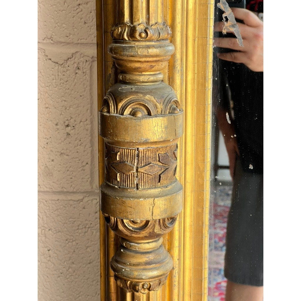 Close-up of an Exceptional Monumental Victorian Renaissance Revival Pier Mirror, circa 1870–1885, featuring an ornate giltwood frame with decorative carvings; part of a person's reflection—revealing their arm and shorts—can be seen in the mirror.
