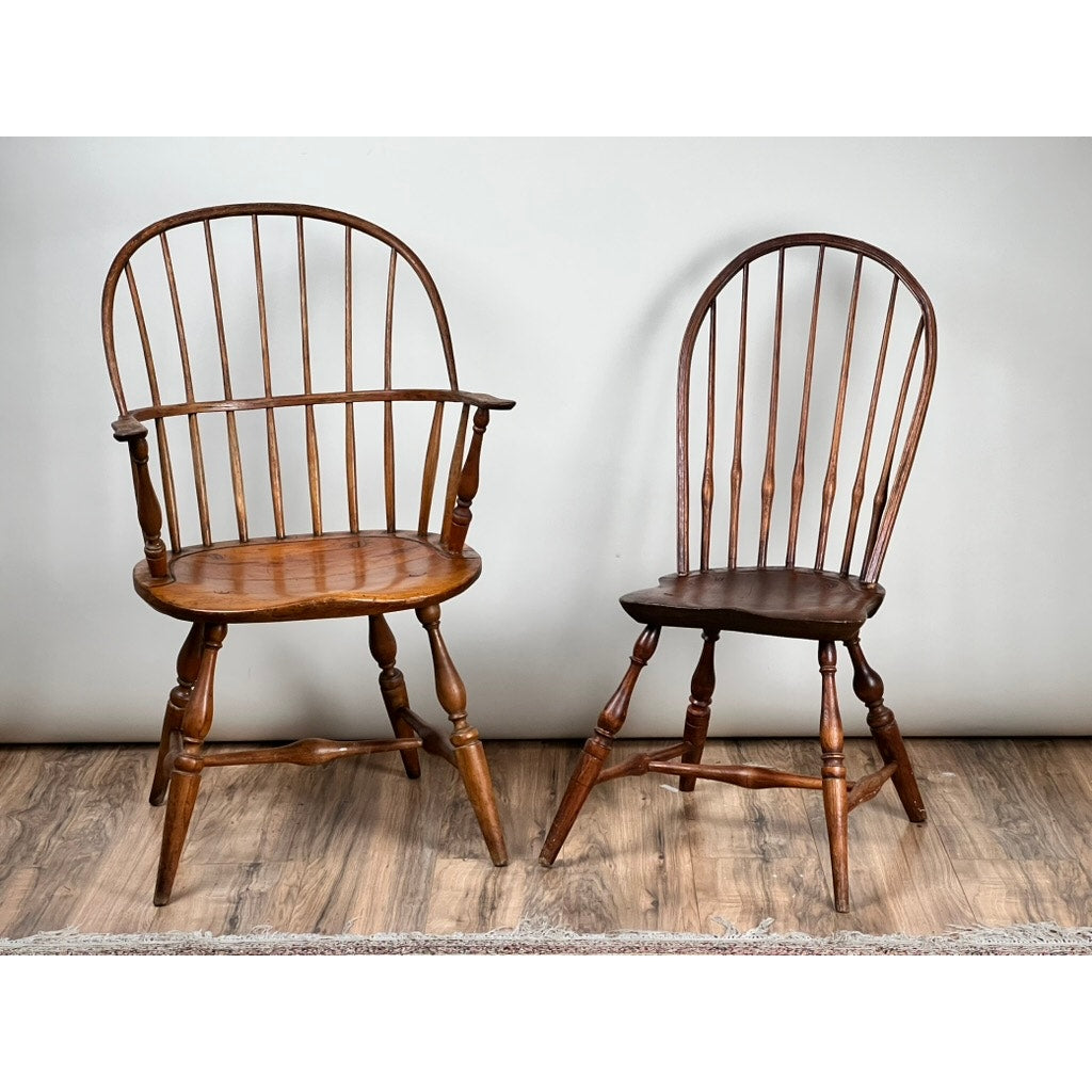 The Antique Near Pair 18th Century Windsor Chairs showcase early American craftsmanship with spindle backs and curved seats; one features armrests, while the other presents a simpler design.
