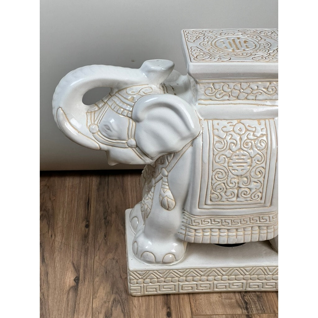 This Vintage Pair White on White Glazed Hollywood Regency Style Elephant Garden Seats features intricate embossed patterns, shown on a wooden floor against a plain light-colored wall. Brand: None/Unknown.
