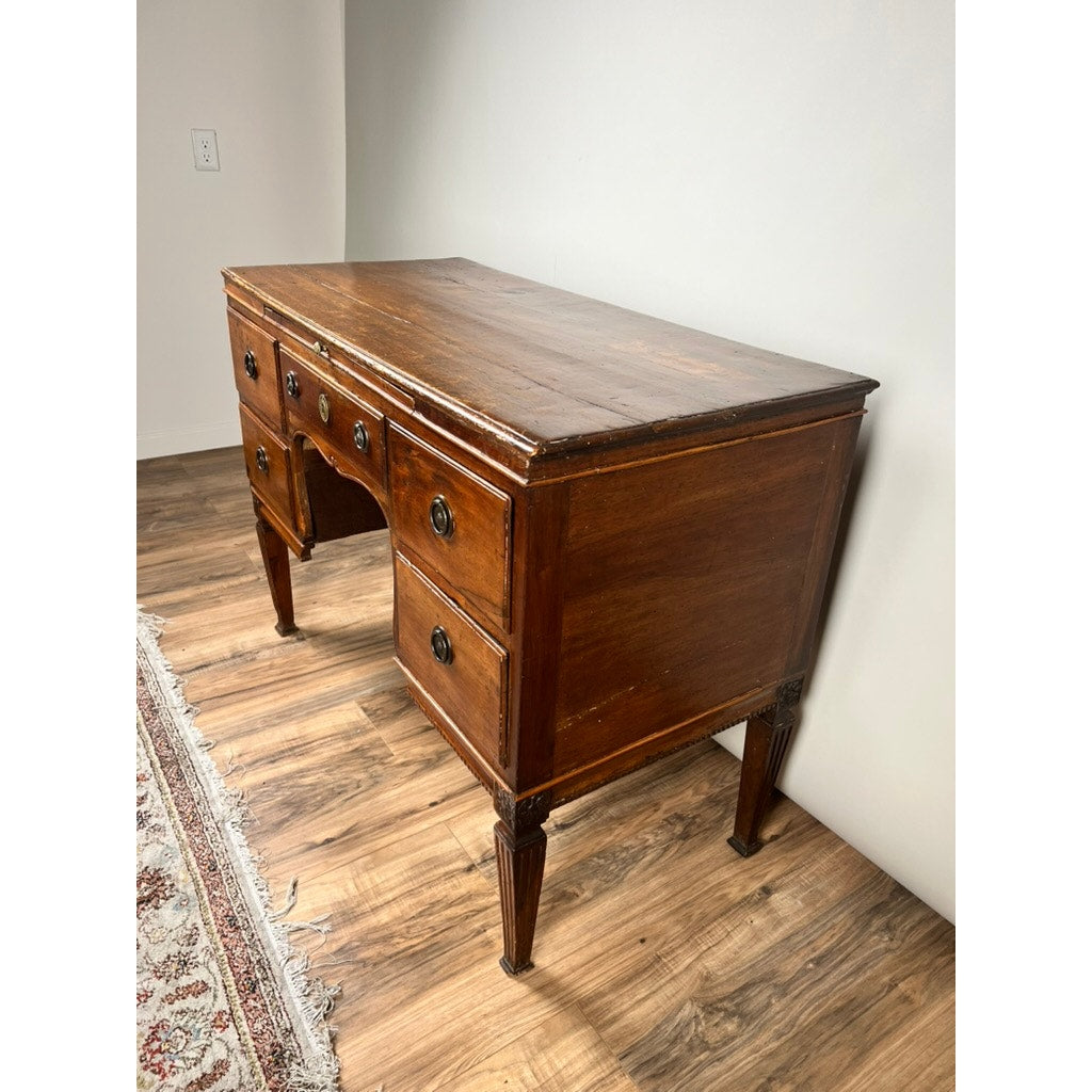 An Antique Louis XVI Period Ladies Desk with a tooled leather top (c. 18th century) stands on a wood floor near a patterned rug and plain white wall—an elegant nod to neoclassical furniture design.