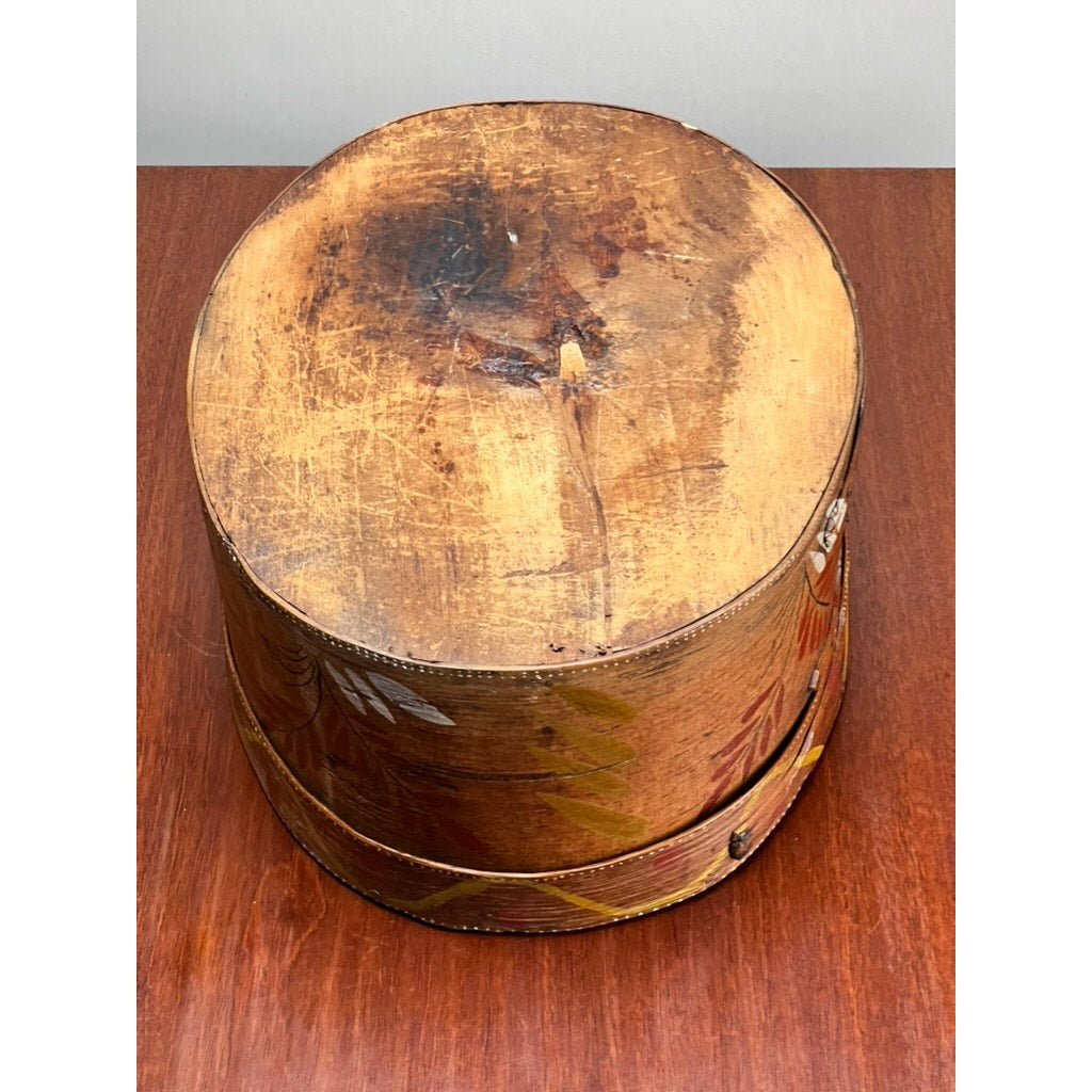 An Antique Swedish Polychrome Painted Marriage Box dated 1798, with a worn lid and faded folk art designs, sits on a reddish-brown wooden surface, reflecting its vintage Scandinavian heritage.
