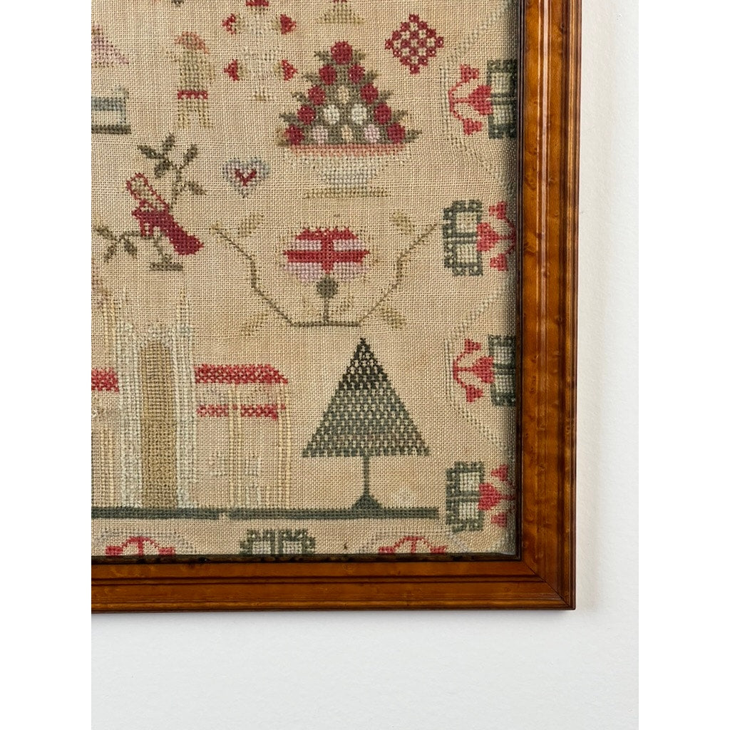 A close-up of an exceptional English Regency schoolgirl needlework sampler by Charlotte Rees, age 11, dated 1816, framed and displayed against a white wall; the antique sampler features geometric and floral patterns in red, green, and beige threads on fabric.