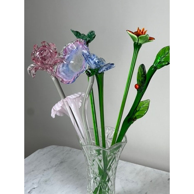 A Vintage Bouquet Murano Art Glass Long Stem Flowers and Butterflies arrangement features colorful glass blooms and butterflies with green stems, displayed in a clear vase on white marble against a neutral background.