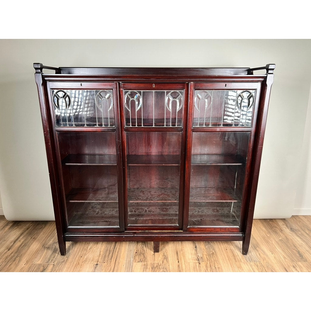 The Antique Arts & Crafts Leaded Glass Mahogany Bookcase c. 1920 features three glass doors with decorative leaded panels, two interior shelves, and a rich, dark finish—an elegant vintage piece for any space. Brand: Unknown.