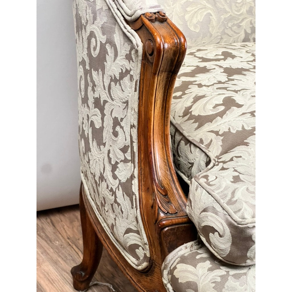 Close-up of the carved walnut armrest on an Antique French Louis XV Rococo Style Bergère Arm Chair c. Mid 19th Century, featuring newer damask upholstery, set on a wooden floor. Brand: None/Unknown.