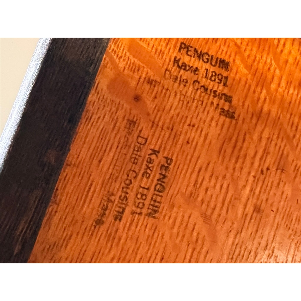 Close-up of a wooden surface, likely from an Antique Hale System Quarter-Sawn Oak Five-Stack Barrister Bookcase (c. 1910) by Camden Cabinet Company, showing black ink stamps reading PENGUIN, Kaxe 1891, and Dale Cousins (appearing twice). The distinctive oak grain and corner edge detail are clearly visible.