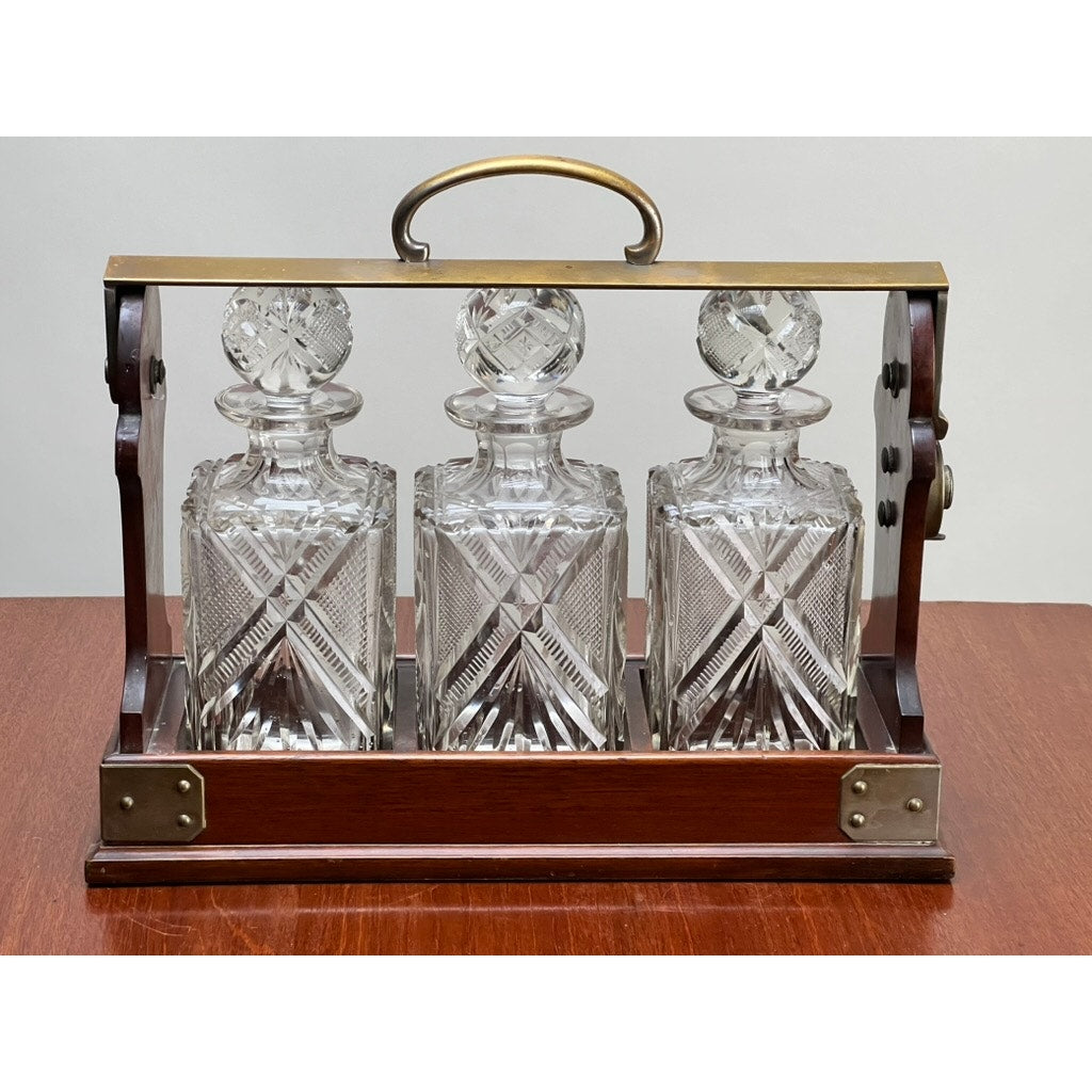 Three cut crystal decanters with stoppers are displayed side by side in an Antique English Edwardian Betjemann’s Three Bottle Tantalus, c. Early 20th Century, set on a polished wooden surface.