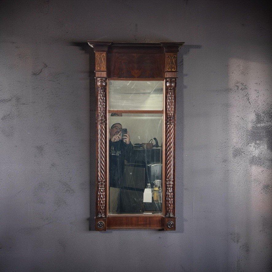 A person takes a selfie in an Antique American Empire Mahogany Pier Mirror c. 1840, mounted on a dark textured wall, with shelves and objects visible in the reflection. Brand: None/Unknown.