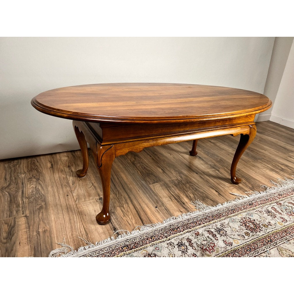 A Vintage Solid Cherry Queen Anne Style Coffee Table (attrib. Pennsylvania House) with curved legs and polished finish stands on a wood floor beside a patterned rug, classic design highlighted by neutral walls.