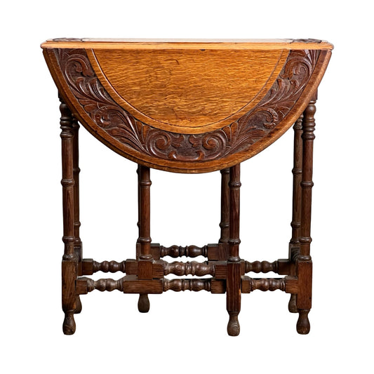 The Antique English Oak Carved Gateleg Occasional Table, c. late 19th century, features ornate carved fold-down sides and elegantly turned legs, shown against a white background. Brand: None/Unknown.