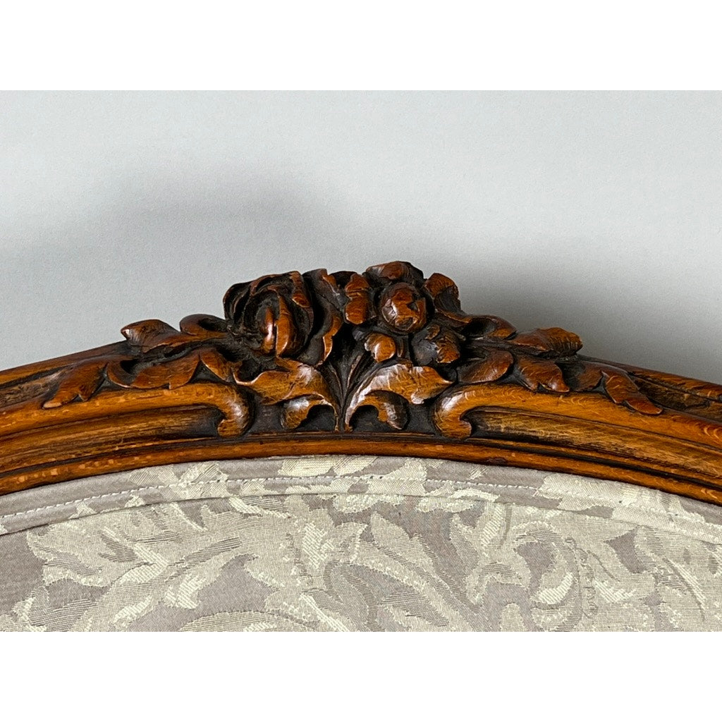 Close-up of a carved walnut floral detail on an Antique French Louis XV Rococo Style Bergère Arm Chair (mid-19th c.) with newer damask upholstery in beige leaf motif. Brand: Unknown.