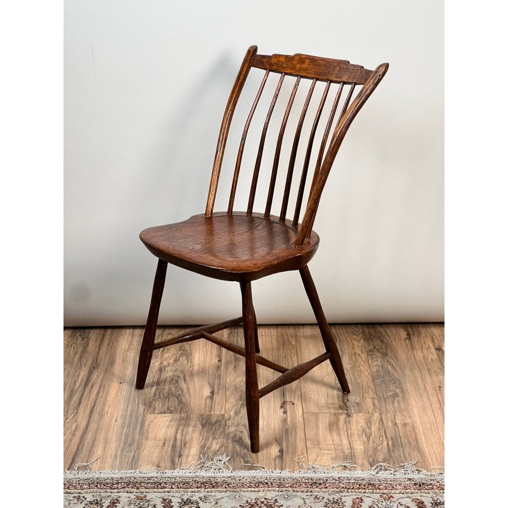 An Antique Step Down Windsor Chair in Oak and Pine (early 19th century) stands on a wooden floor beside a patterned rug, set against a plain light-colored wall. Brand: Unknown.