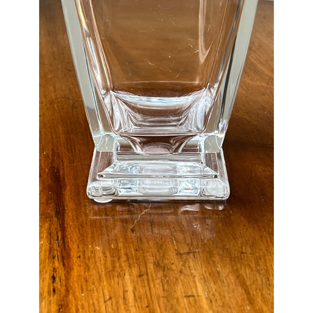 A close-up of the Vintage Baccarat Crystal Pearl Vase by Baccarat, featuring a clear crystal body and square base, rests on a warm brown wooden surface with visible grain.