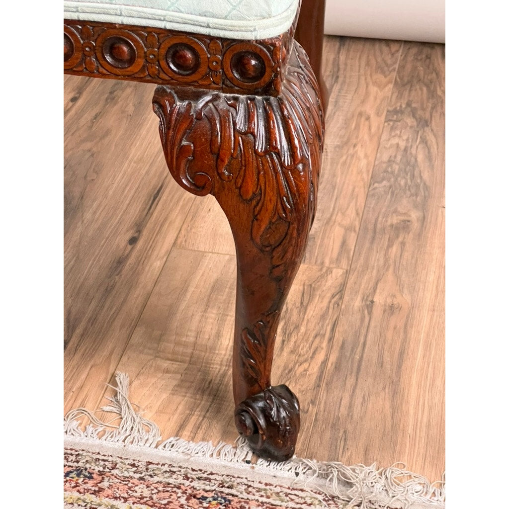 Close-up of an Antique George II Mahogany Gainsborough Open Arm Chair (mid-19th century), highlighting its ornate carved cabriole legs with claw feet, set on a wooden floor beside the fringed edge of a patterned rug.