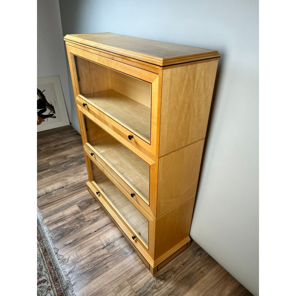 A Vintage Bench Made Maple with Wenge Inlay Three Stack Barrister Bookcase stands against a light wall on a wood floor, positioned beside framed artwork and the edge of a patterned rug.