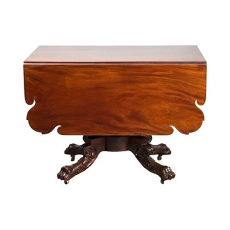 American Classical Carved Mahogany Drop-Leaf Breakfast Table, c. 1825–1840, featuring a center pedestal base with carved animal paw feet and casters.