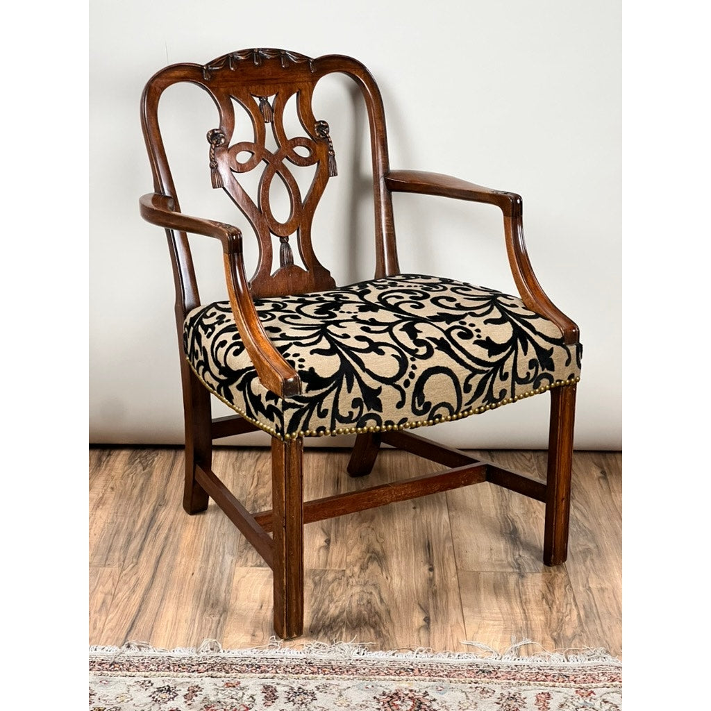 An Antique George III Chippendale Open Arm Chair (Early 19th Century), featuring a carved back and black and beige damask upholstered seat, sits on a wooden floor beside a patterned rug. Brand: None/Unknown.
