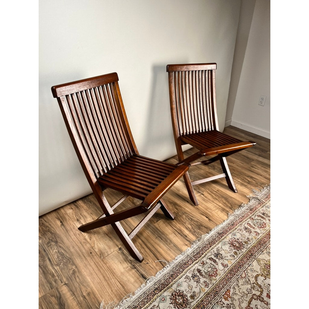 A Pair of Vintage Mid-Century Modern Style Teak Folding Chairs are set side by side on a wooden floor, adjacent to a patterned rug and a plain light-colored wall. Brand: None/Unknown.