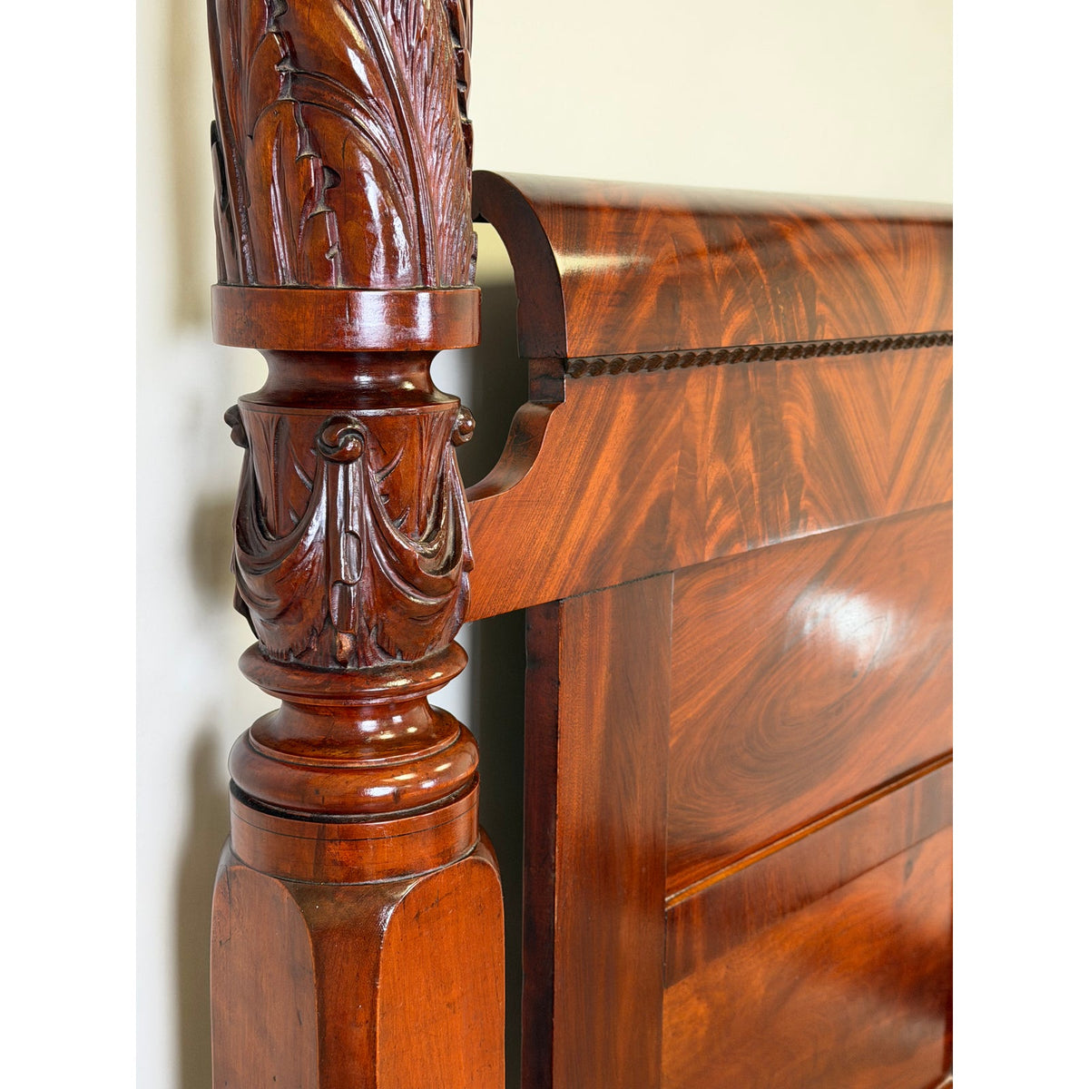 Close-up of an American Classical Carved Mahogany Four-Poster Tester Bed, possibly New York, circa 1825–1840, featuring an ornate botanical mahogany bed post next to a polished, curved headboard.