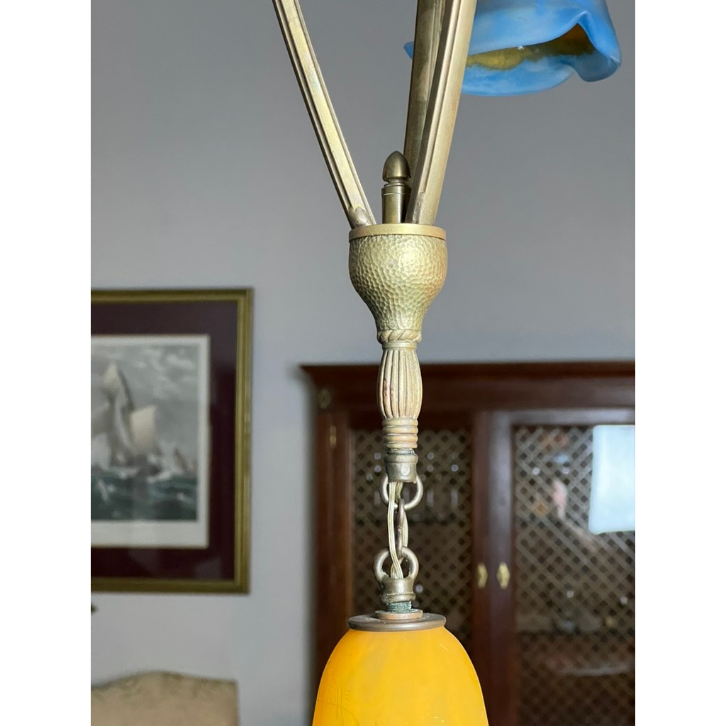 A close-up of the Vintage Muller Frères Lunéville French Brass and Art Glass Four Light Chandelier, featuring a yellow Art Nouveau glass shade, with a framed ship picture and wooden cabinet in the background.