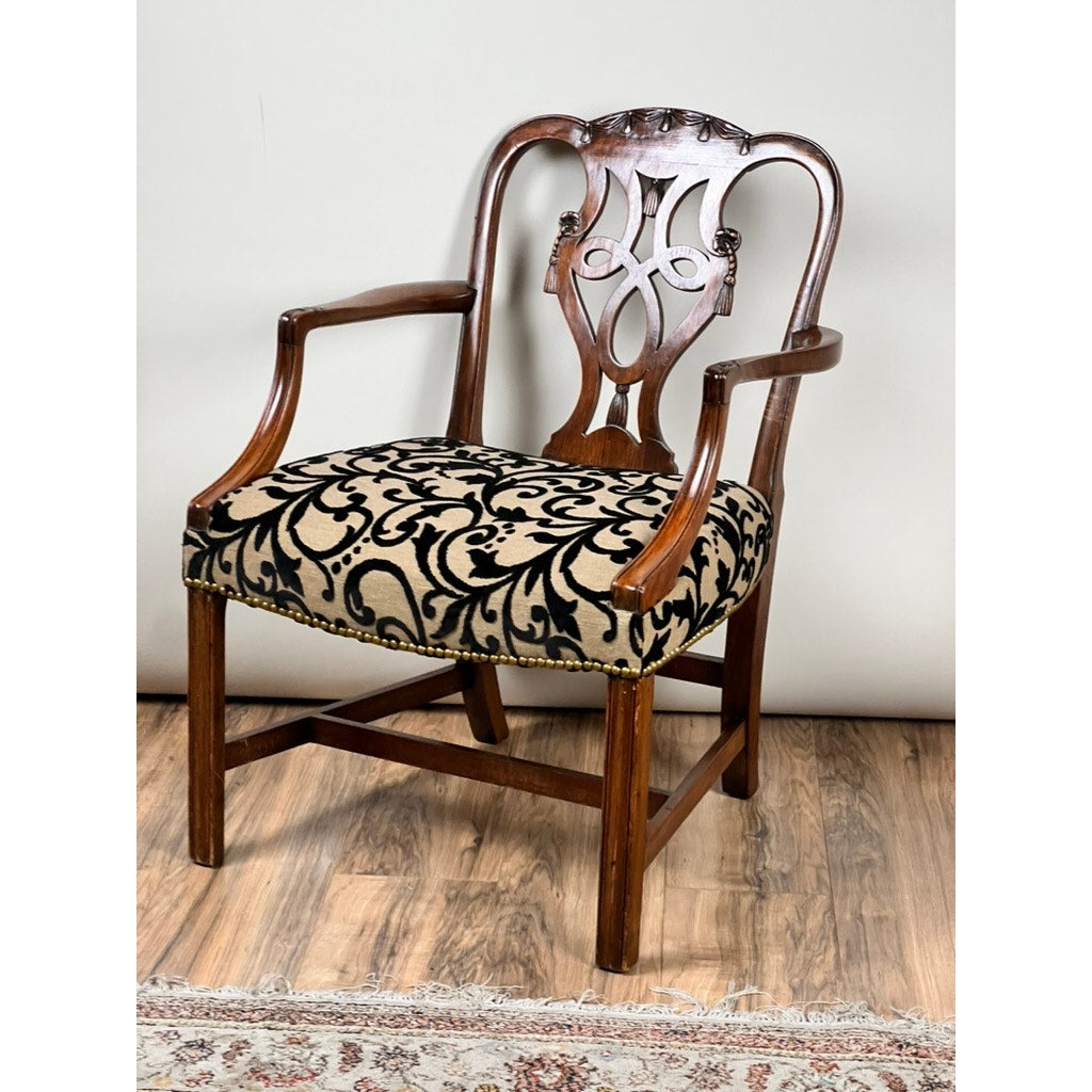 An Antique George III Chippendale Open Arm Chair (early 19th century) features an ornate carved backrest, curved arms, and a beige seat with a bold black floral pattern. This English antique rests on a wooden floor beside a patterned rug.