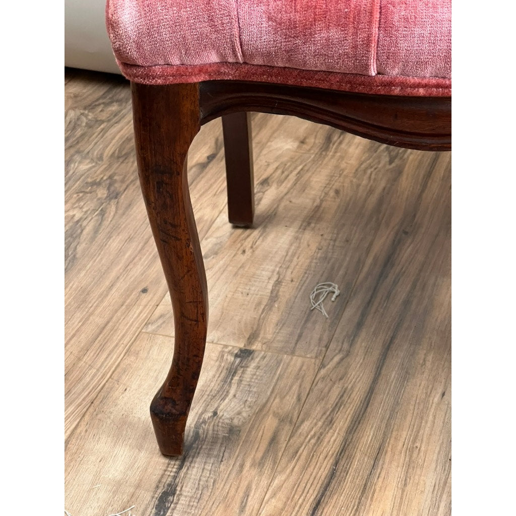 A close-up of an Antique Pair Victorian Walnut Balloon Back Tufted Side Chairs (Late 19th Century) shows a curved chair leg supporting faded pink upholstery, with the chair set on a light brown wood floor where a small string is visible.