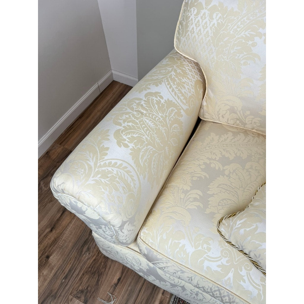 A close-up of the Vintage Custom Ivory Upholstered Sofa by Stickley, featuring a floral damask pattern, is shown on a wooden floor near a white wall and corner.