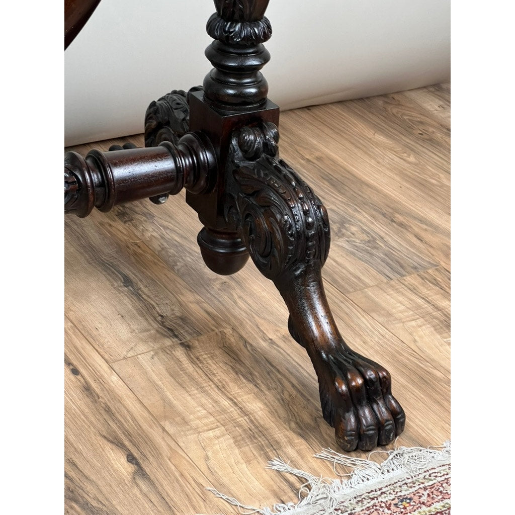 Close-up of an ornately carved animal paw table leg, echoing details on the Impressive Antique American Empire Acanthus and Barbola Rose Carved Cheval Mirror c. 1840, resting on wood flooring beside a patterned rug.
