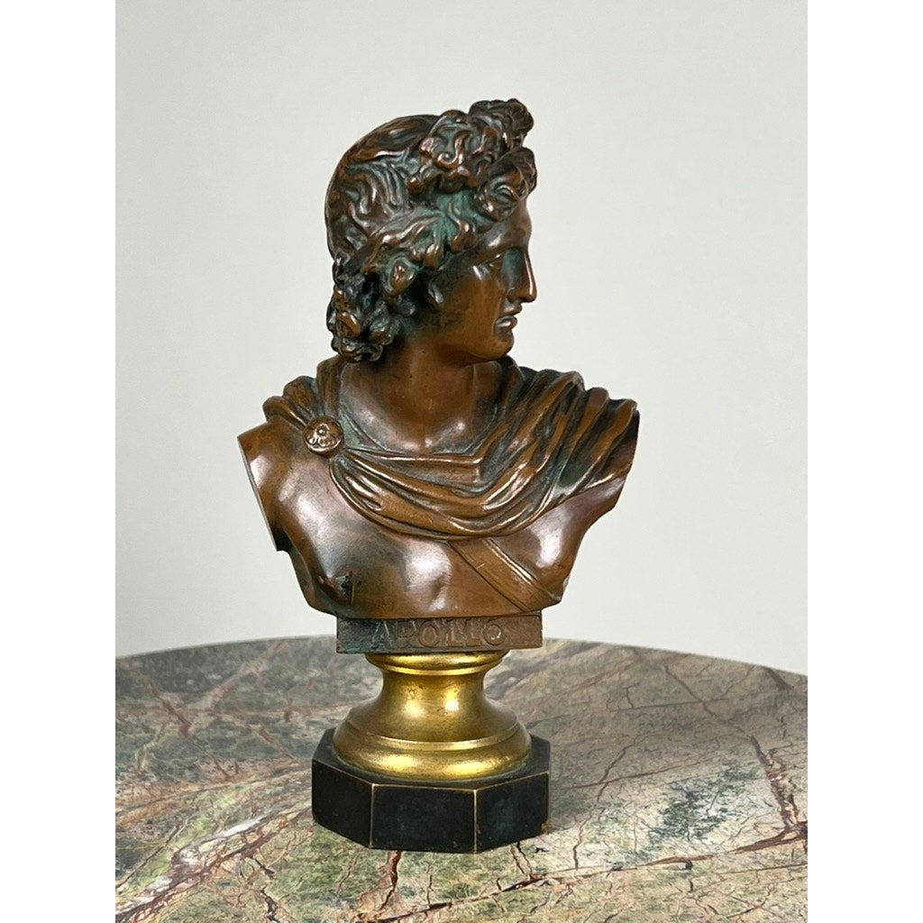 An Antique Small Bronze of “the Apollo Belvedere” with Vienna Foundry Mark features curly hair and draped robes on a round pedestal atop a map-like surface, highlighting neoclassical style against a plain backdrop. Brand: unknown.