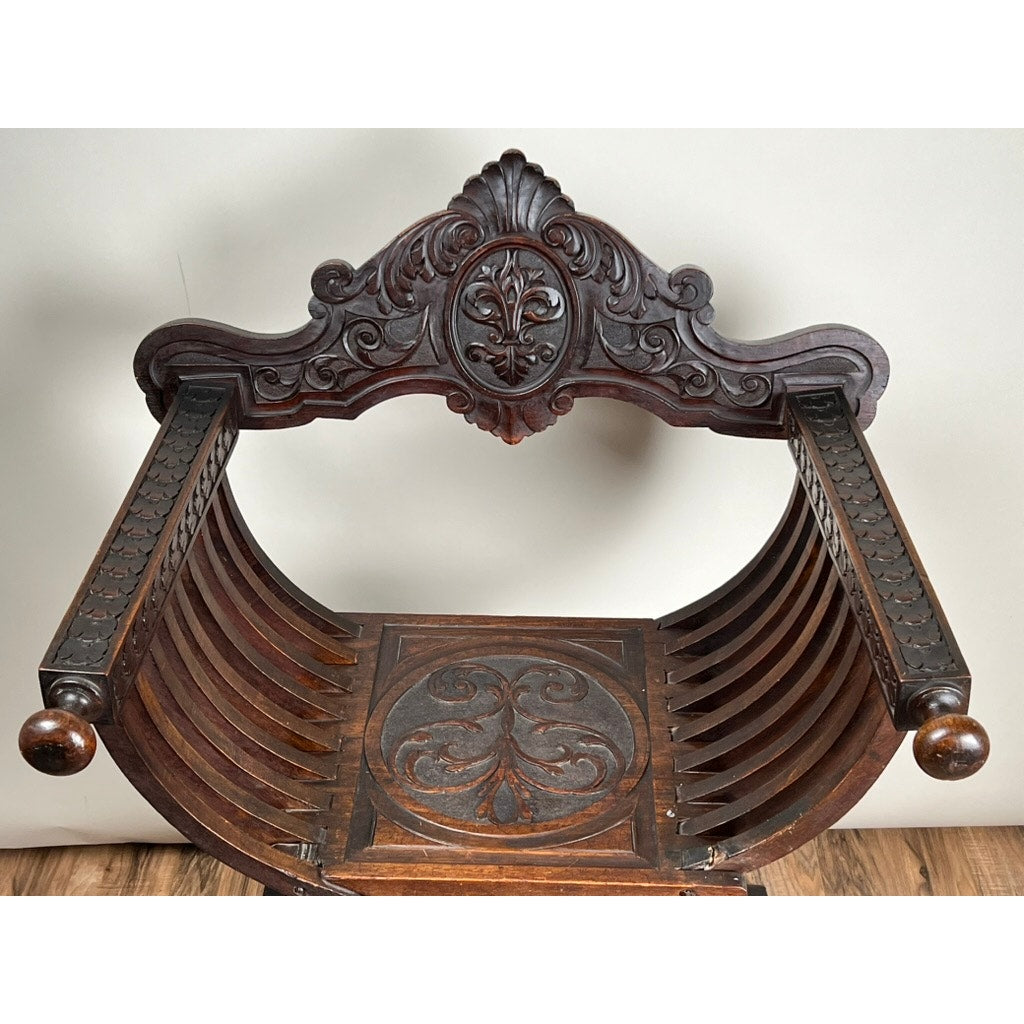 The Antique Italian Renaissance Walnut Savonarola Chair (c. Late 19th Century) features curved slatted sides, intricate scrollwork, and decorative floral patterns, elegantly displayed on a wooden floor.
