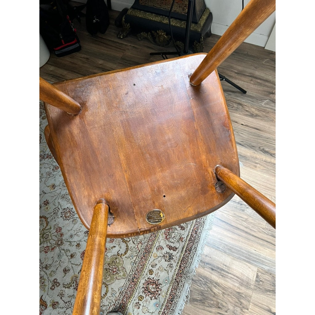 A Vintage Herman DeVries for Cushman No. 5-82 Rock Maple Easy Chair by Cushman is upside down on a patterned rug, revealing its seat and legs, with a wooden floor and musical equipment visible in the background.