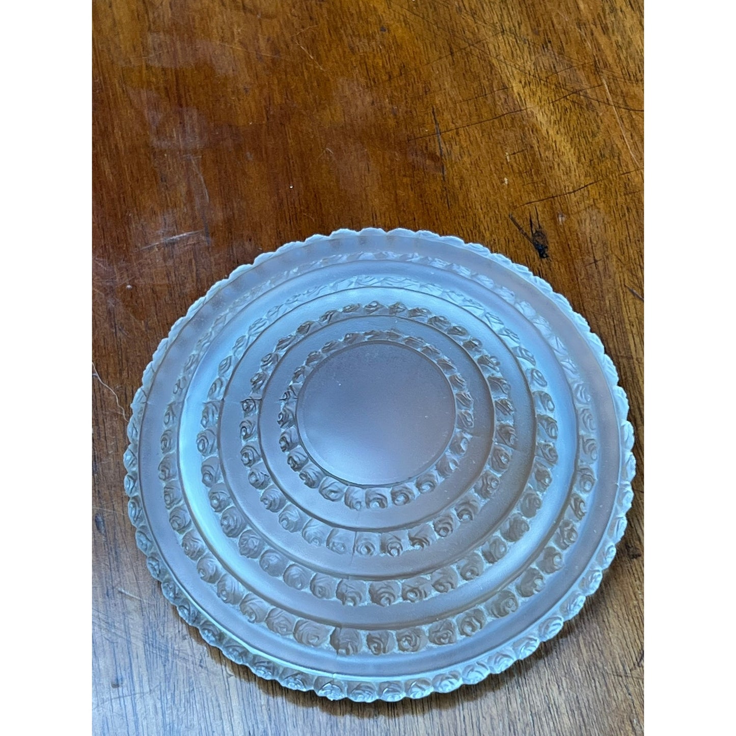 A Vintage Lalique Crystal Enfants Box by Lalique is displayed on a wooden surface, featuring ornate circular designs and a scalloped edge reminiscent of French art glass.