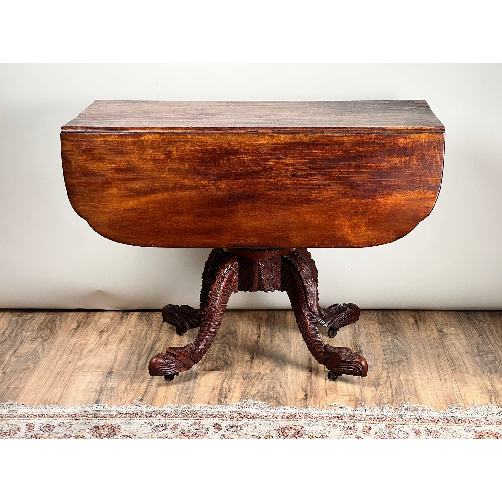 An Antique American Empire Drop Leaf Table with Great Eagle Carved Feet c. 1840 stands on a hardwood floor, with part of a patterned rug visible at the bottom of the image. Brand: None and/or Unknown.