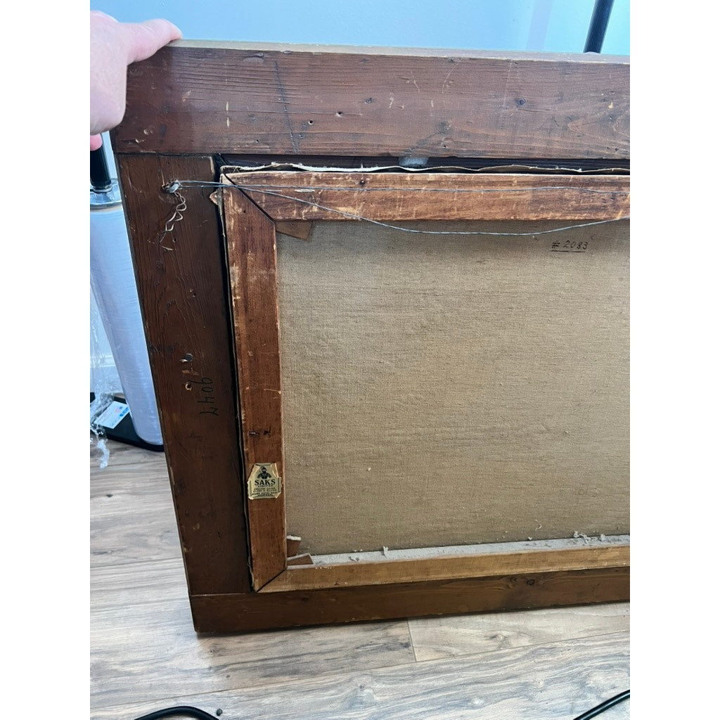 The photo shows the back of an early 20th-century "Path by a Stream" oil on canvas, signed P. Grabwin. A hand holds the frame, exposing old nails, a worn canvas edge, and a triangular label—all resting on a wooden floor. Brand unknown.