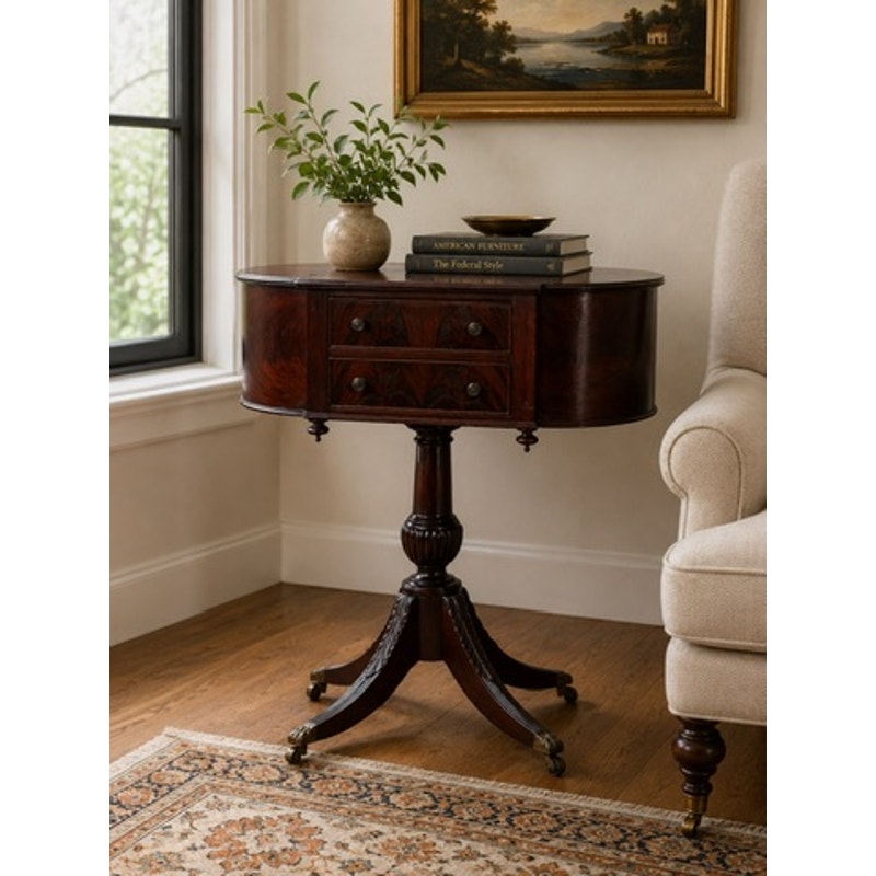 An Early 19th Century New York Classical Mahogany Astragal-End Work Table in the manner of Duncan Phyfe (c. 1815–1825) stands beside a beige armchair on a patterned rug, adorned with books, a bowl, and a potted plant, near a window in an inviting and elegant room.