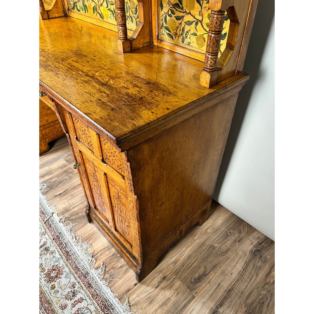 Antique Victorian Aesthetic Movement oak desk in its original late 19th-century finish, featuring ornate carved details and brass handles, stands on a wood floor by a white wall and a fringed patterned rug for timeless charm.
