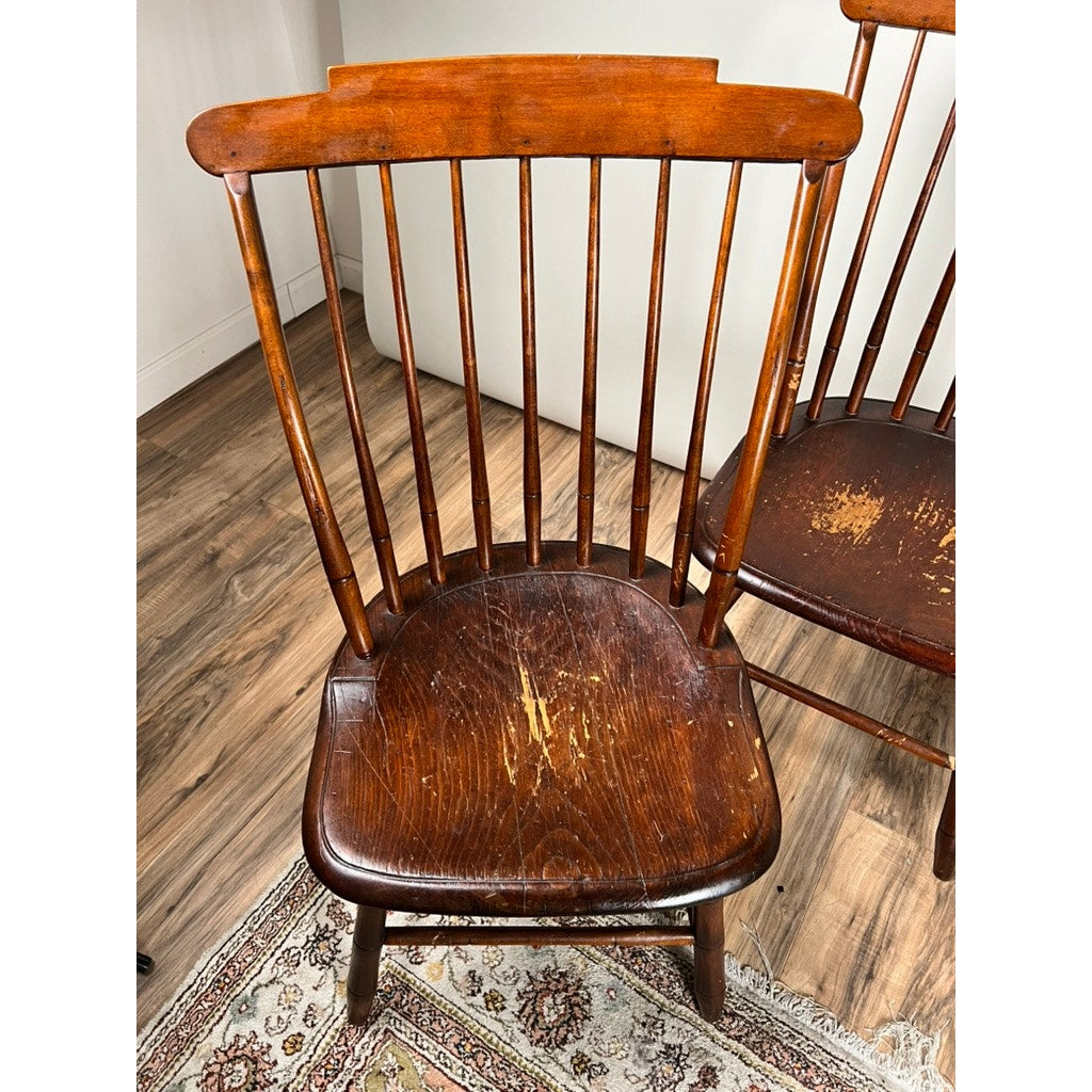 A set of four early 19th-century JR Hunt New Hampshire Step Down Windsor Chairs, signed by J.R. Hunt, display visible seat wear and scratches. The chairs are placed on a patterned rug atop hardwood flooring.