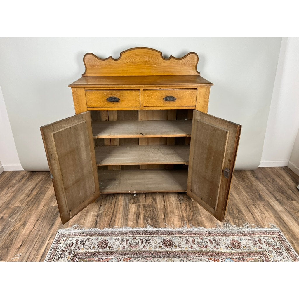 The Antique Victorian Grain Painted Country Jelly Cupboard c. 1870 features a decorative back, two drawers, cabinet doors with three shelves, and stands on a wood floor next to a patterned rug and plain white wall.