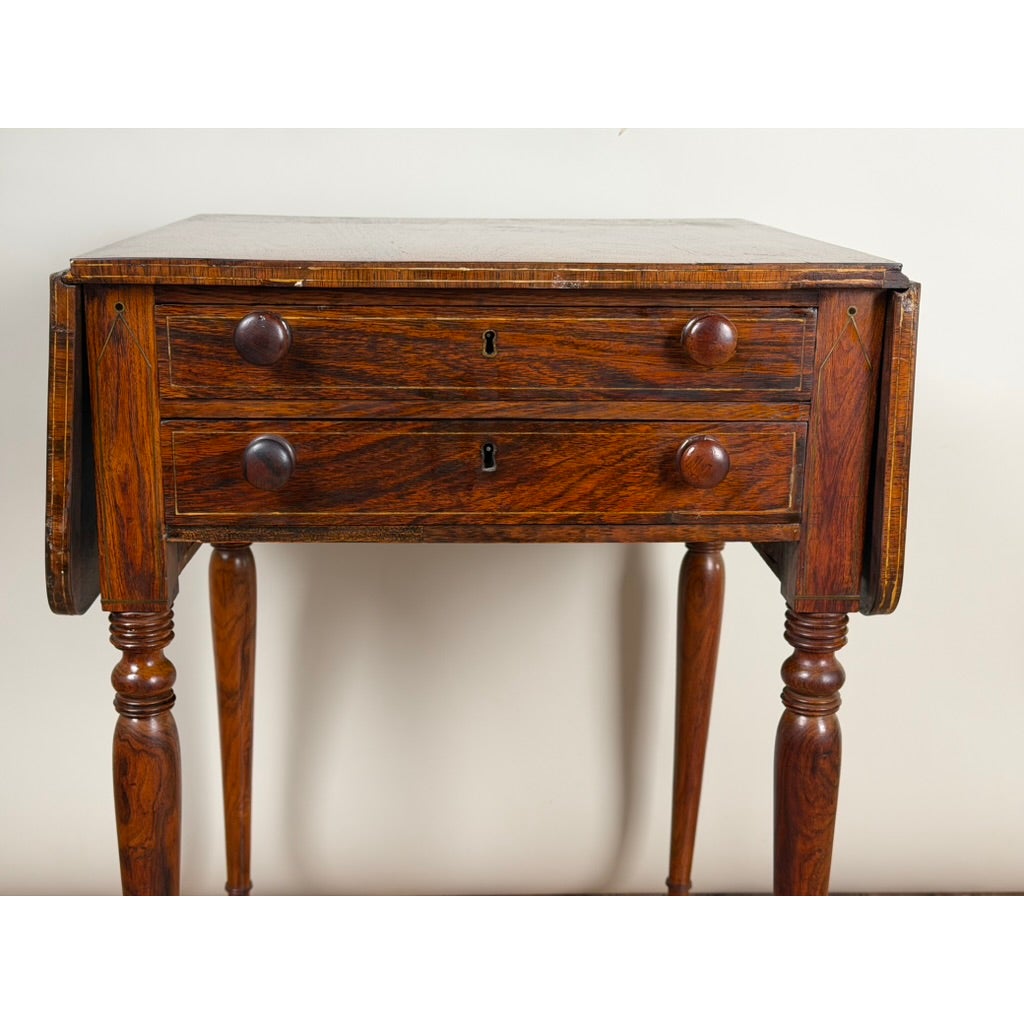 English Regency Rosewood Two-Drawer Drop-Leaf Work Table with Brass and Satinwood Inlay by Pearl City Antiques, featuring dark rosewood grain, brass inlay accents, two drawers, and turned legs.