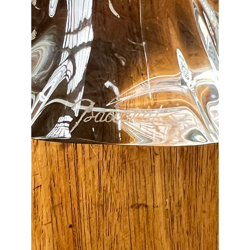 Close-up of a Vintage Baccarat Crystal Angel by Baccarat, with the brand name engraved on it, resting on wood. Light reflects off the crystal, creating captivating patterns.