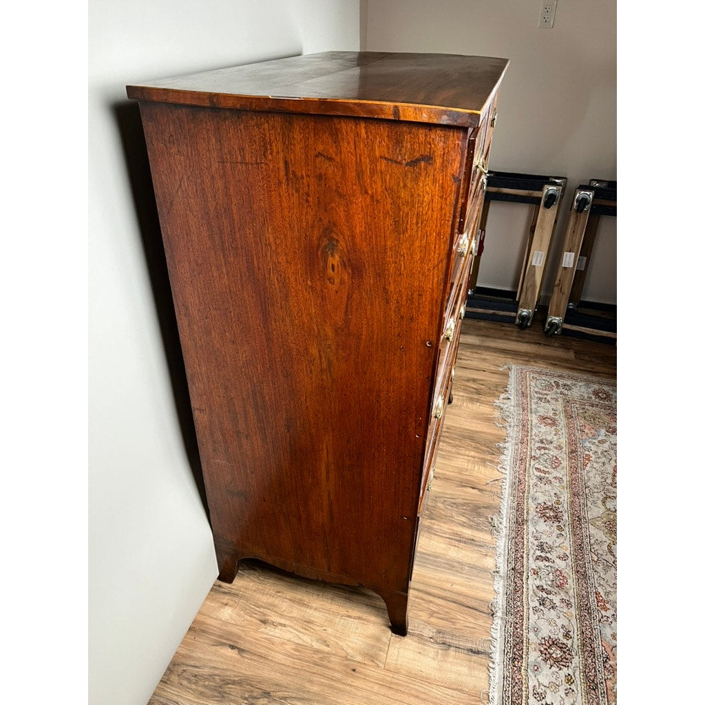 An Antique George III Two Over Four Chest with French Feet (c. Early 19th Century) stands on a hardwood floor beside a patterned rug and blank wall, its polished wood grain and brass drawer handles captured in a side view. Brand: Unknown.