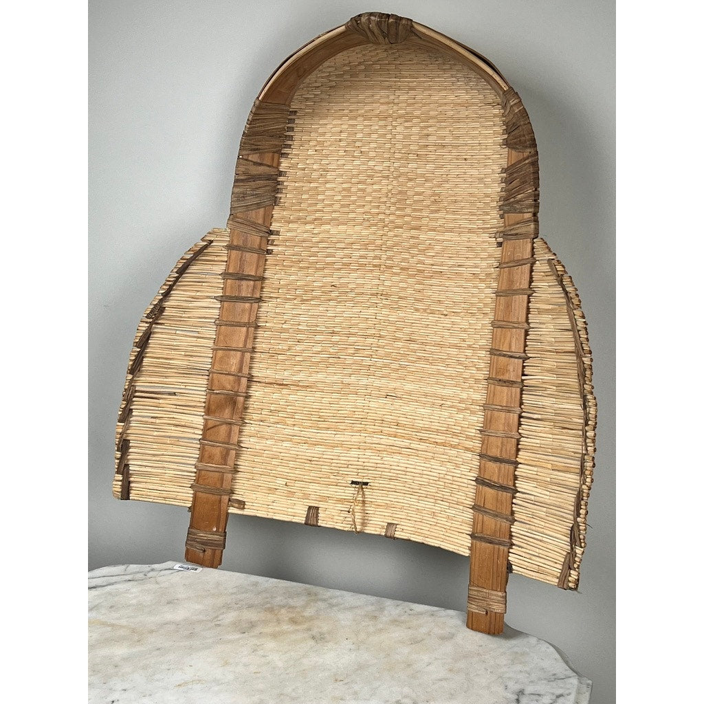 The Vintage Traditional Winnowing Basket, made from natural fibers with a curved top, is shown upright on a light marble surface against a plain gray background—ideal for vintage-inspired decor.