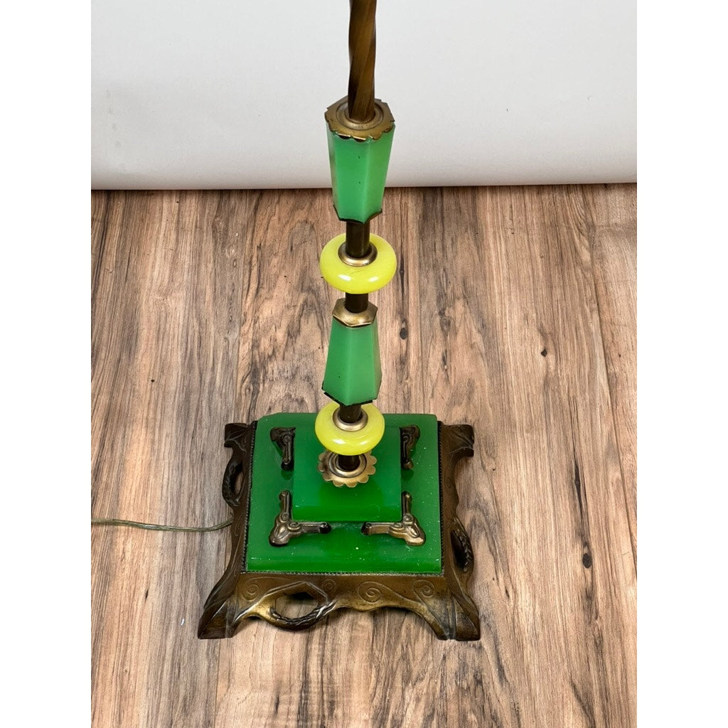 An Antique Art Deco Uranium and Slag Glass Lamp c. 1920 with green and yellow uranium glass base, brass accents, and ornate dark claw feet stands on a wooden floor against a plain white background. Brand: None/Unknown.