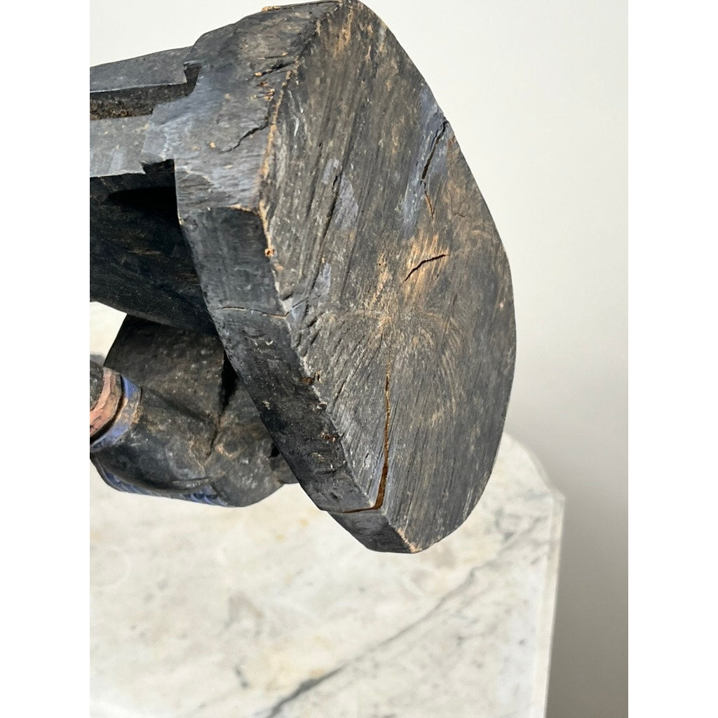 A close-up of the weathered head of an Antique Igbo Ikenga Shrine Figure, probably from Nigeria, with visible cracks and rough texture, resting on a pale, slightly marbled surface. Brand: None or unknown.