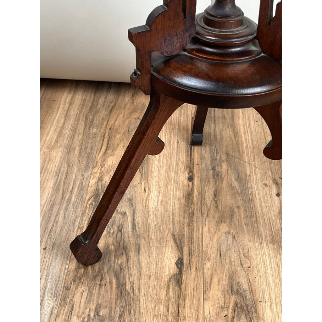 A close-up of a late 19th-century Antique Victorian Walnut Candle Stand shows its ornate wooden leg and part of the seat, set on a light brown finished wooden floor. The brand is unknown.