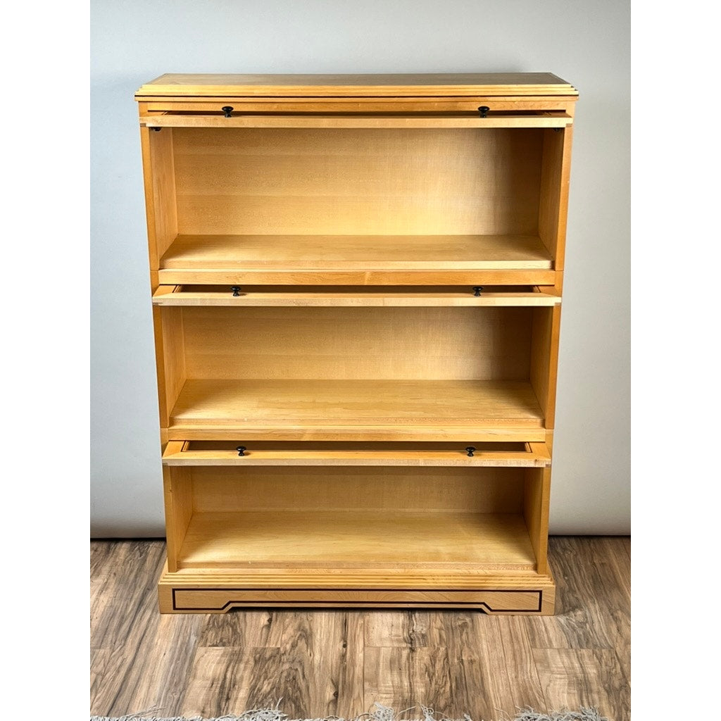 A Vintage Bench Made Maple with Wenge Inlay Three Stack Barrister Bookcase featuring three glass-front panels that lift up and slide in, sits on a wooden base against a light-colored wall on a wooden floor. Brand: None/Unknown.