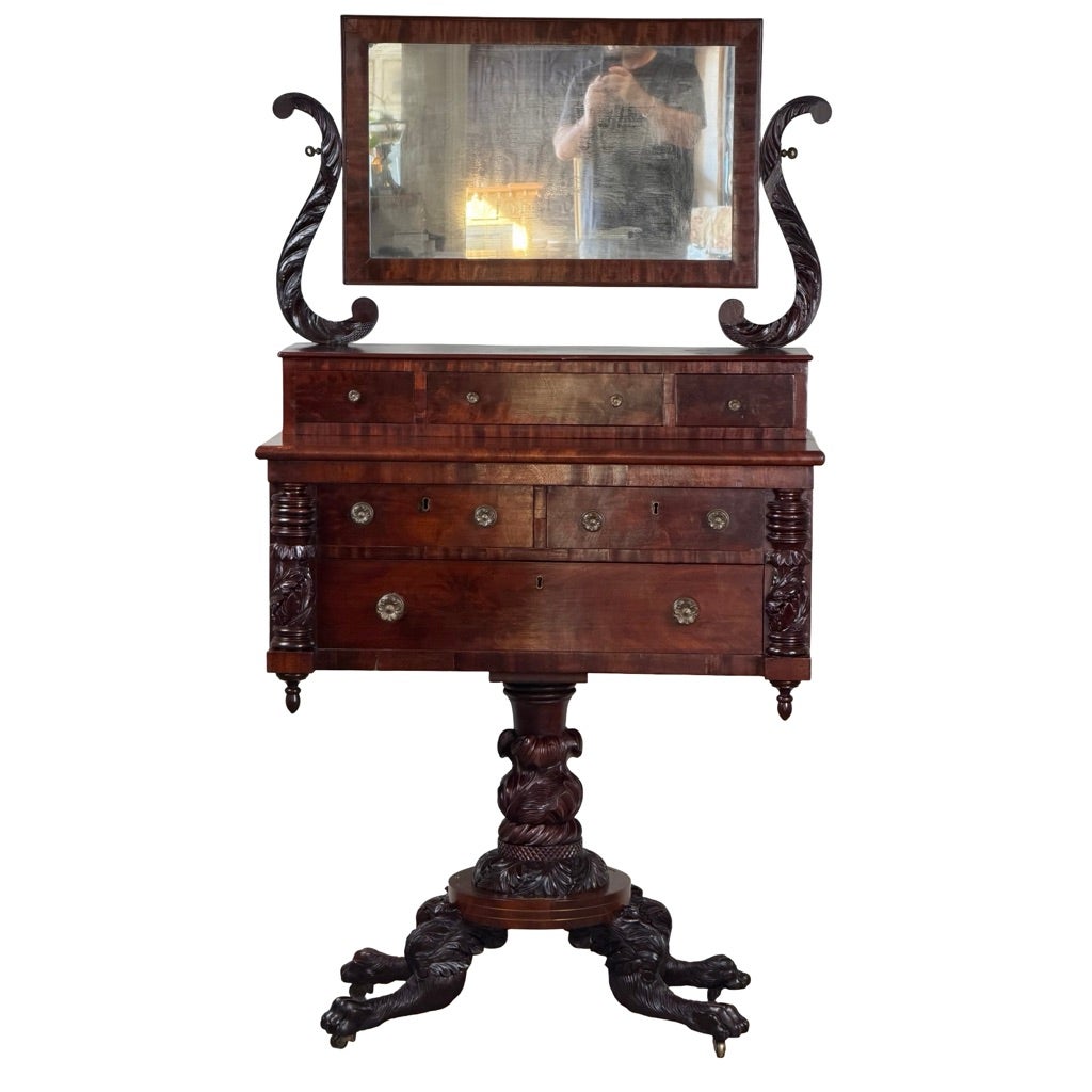 An American Classical Carved Mahogany Dressing Table with Original Mirror, Probably New York, c. 1825–1835, features a rectangular mirror on curved uprights, a drawer cabinet on a pedestal base, and carved claw feet.