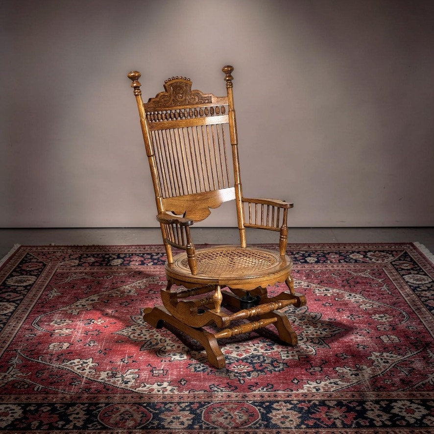 The Antique Victorian Oak Platform Rocker c. Late 19th Century, with woven cane seat and elegant carvings, sits atop a red patterned rug under soft lighting—an ideal choice to enhance any antique furniture collection.