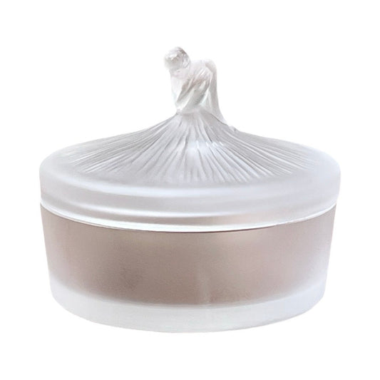 The Vintage Lalique France Ballerina Frosted Crystal Covered Powder Box by Lalique is a round, matte, translucent frosted glass jar with a lid topped by a sculpted ballerina figure as the handle.